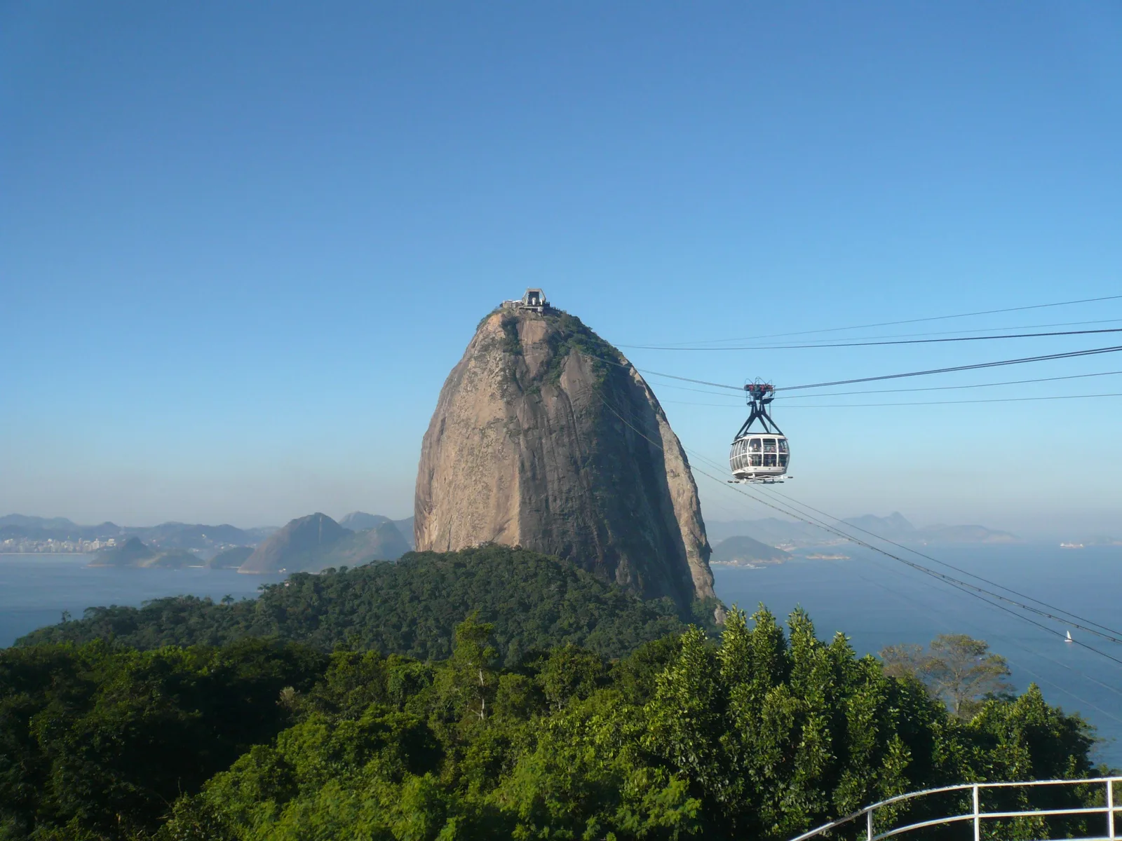 Sugarloaf Mountain rising bare and gray above the forest, a cable car crossing the span toward its summit with Guanabara Bay behind