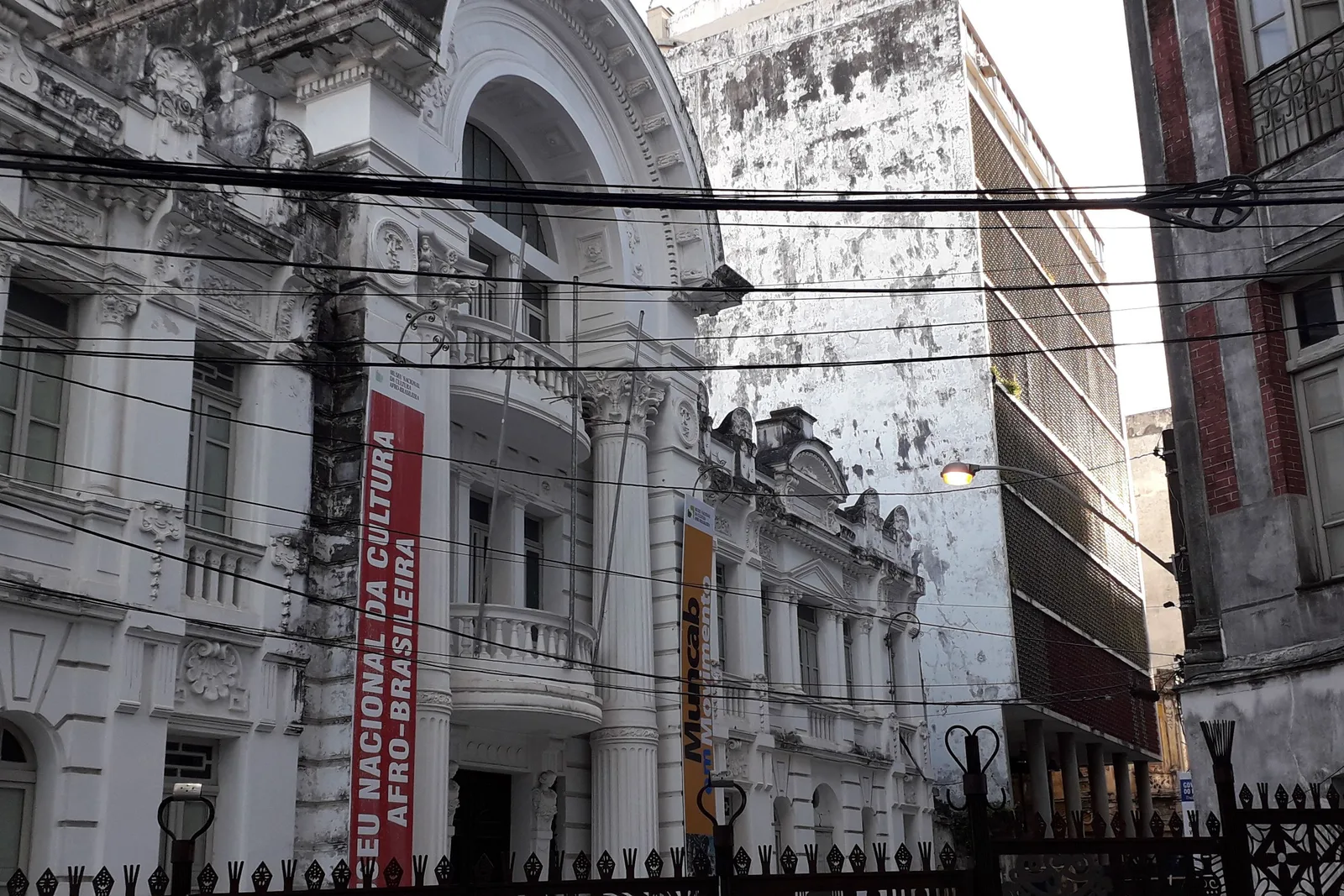 The Museu Nacional da Cultura Afro-Brasileira seen from the street below the Pelourinho: a tall red banner carrying the museum’s name hung down the columned white facade of the restored mansion, a second banner beside it and iron railings along the front