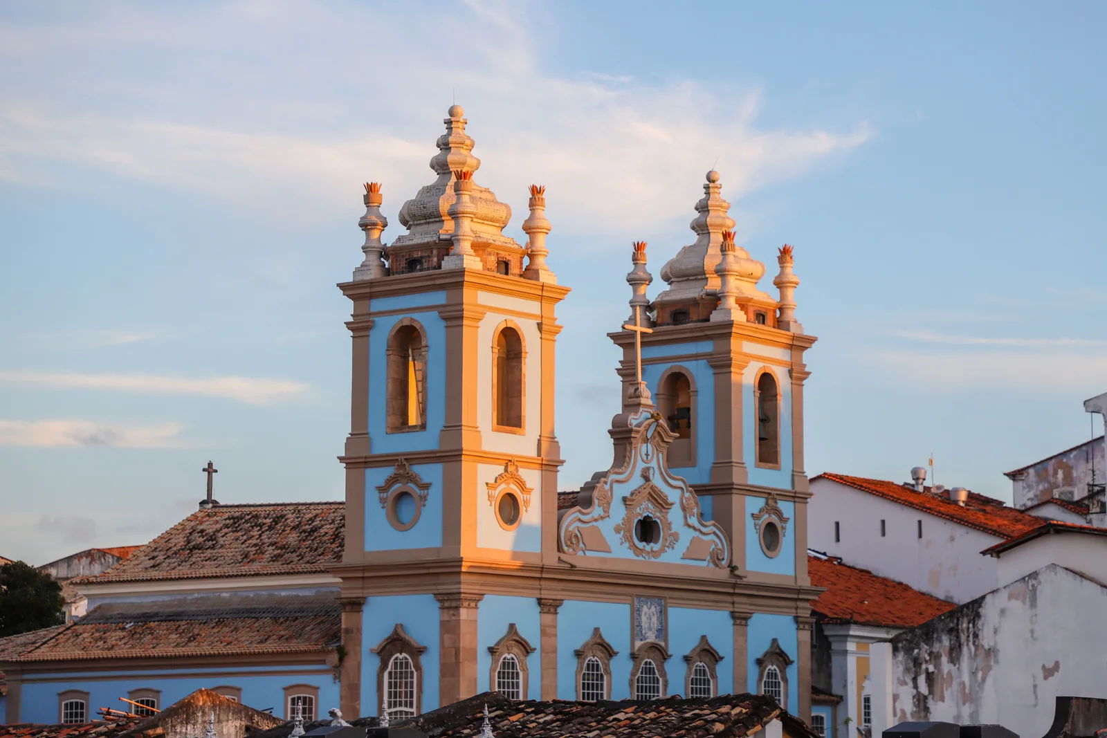The pale blue and white baroque bell towers of the Igreja do Rosário dos Pretos catching the last of the sun, seen over the tiled rooftops of the Pelourinho below