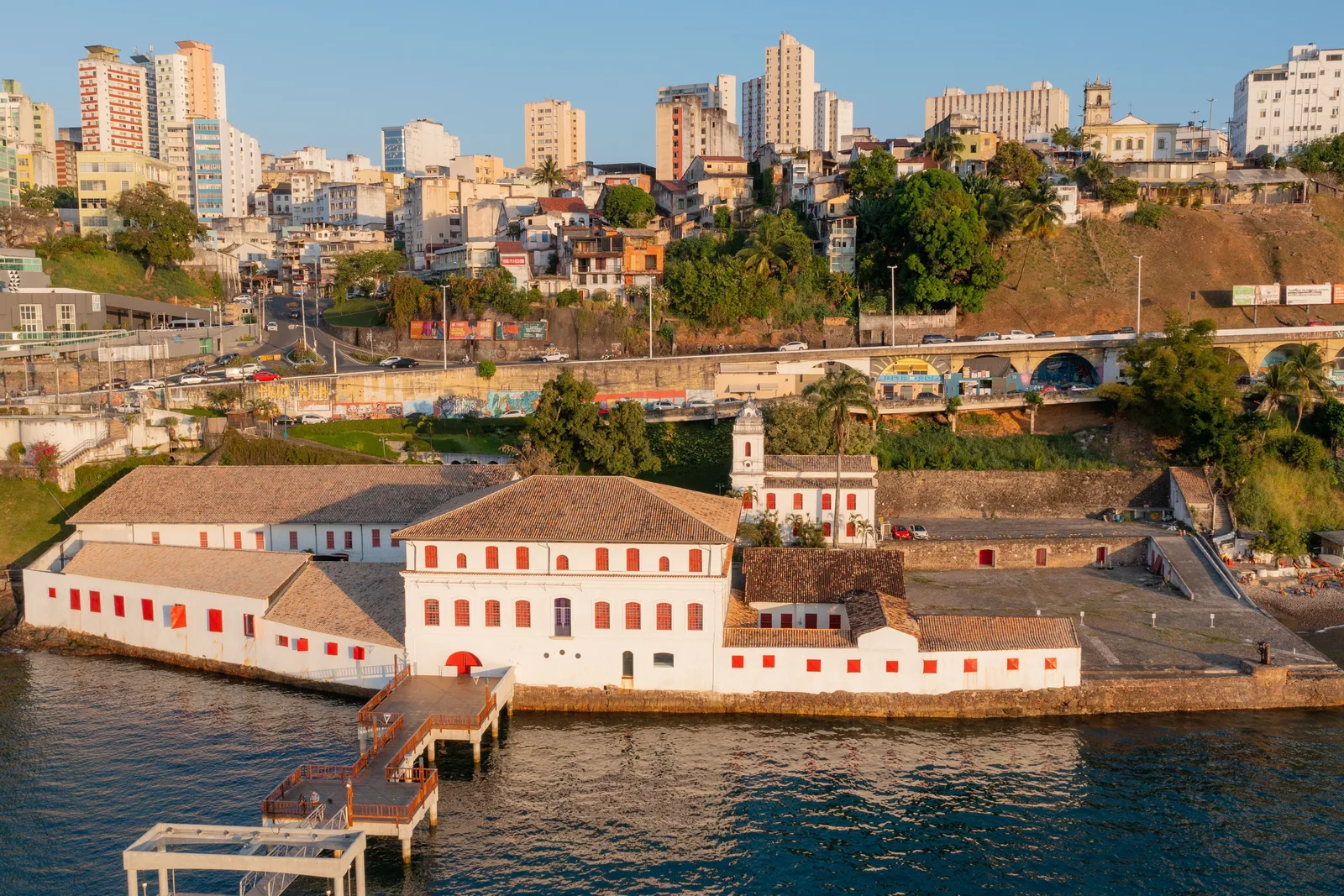 The Solar do Unhão late in the day, seen from over the water: the whitewashed colonial warehouse, chapel and yard of the modern art museum on their own promontory, with the apartment blocks and hillside of the city rising behind