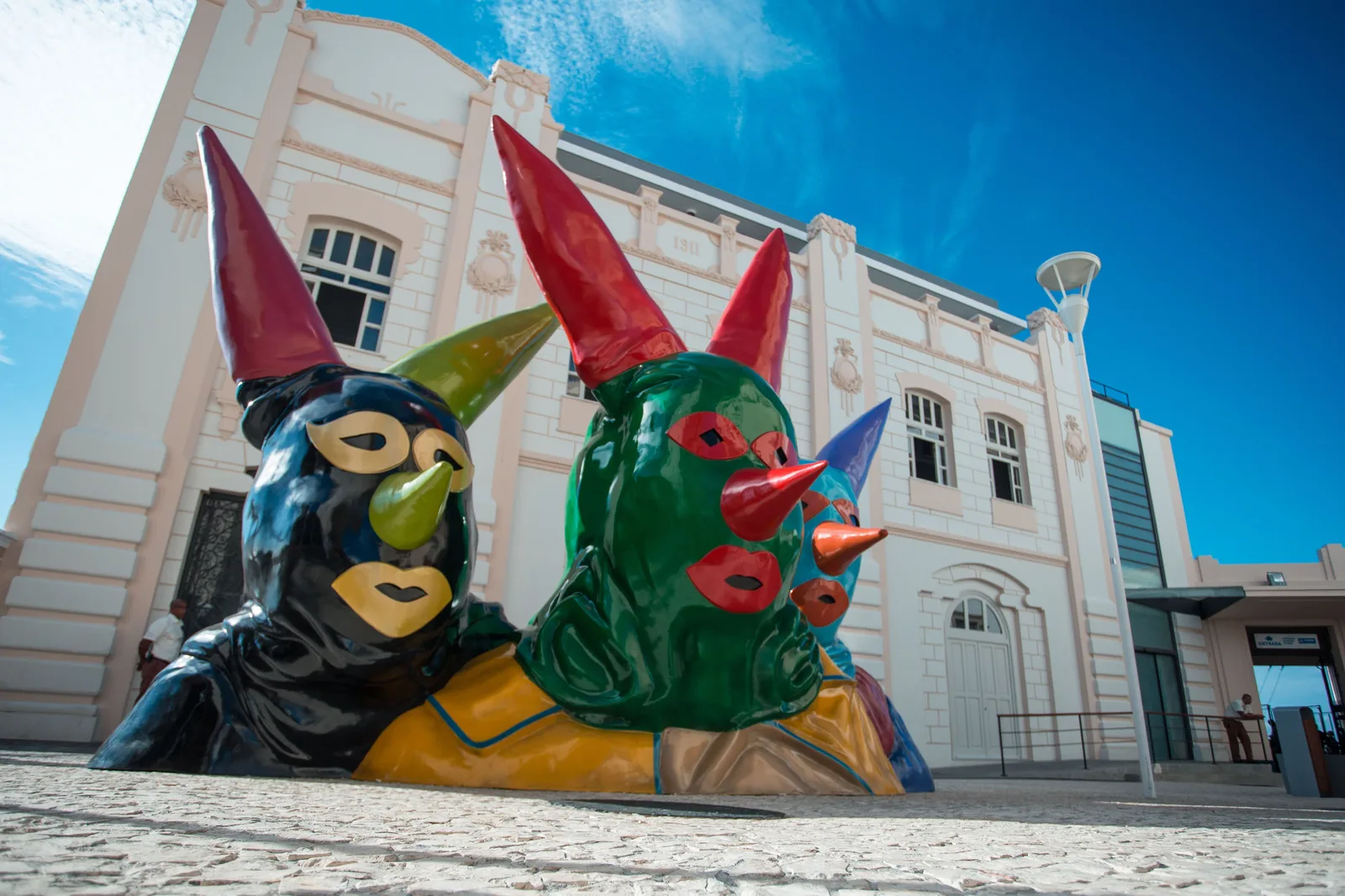 Giant carnival masks with horns and bright paint set out in front of a white building in the Pelourinho