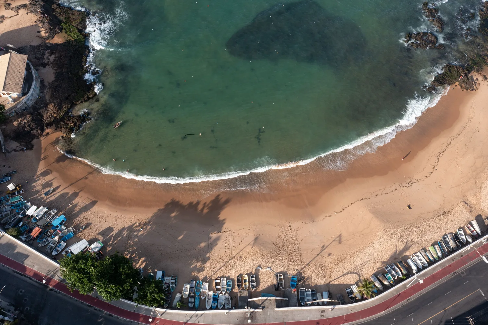 A small crescent beach in Rio Vermelho from above, green water, boats pulled up along the seawall