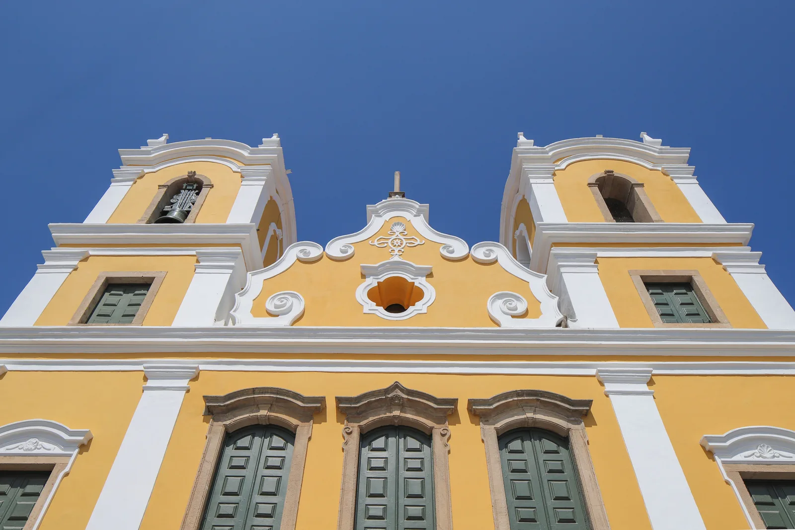 The yellow and white baroque façade of the Igreja da Saúde e Glória against a deep blue sky