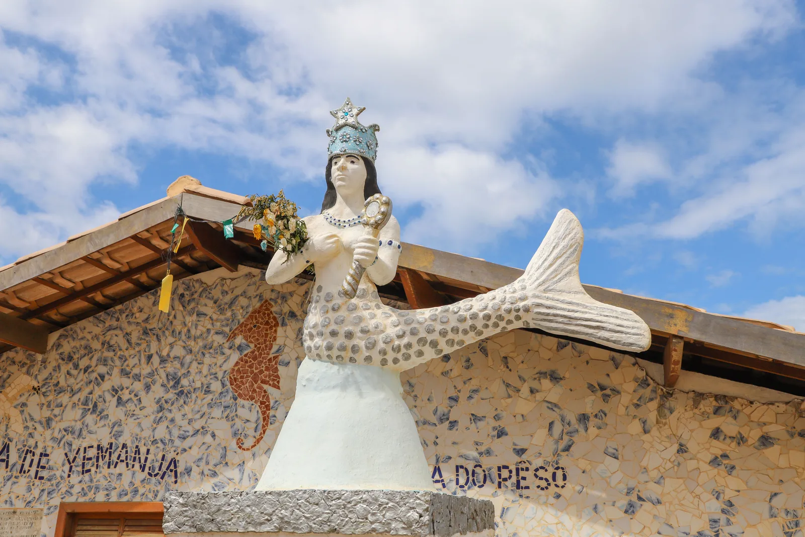 A white mermaid sculpture of Yemanjá, crowned and holding a mirror, on the roof of her house in Rio Vermelho