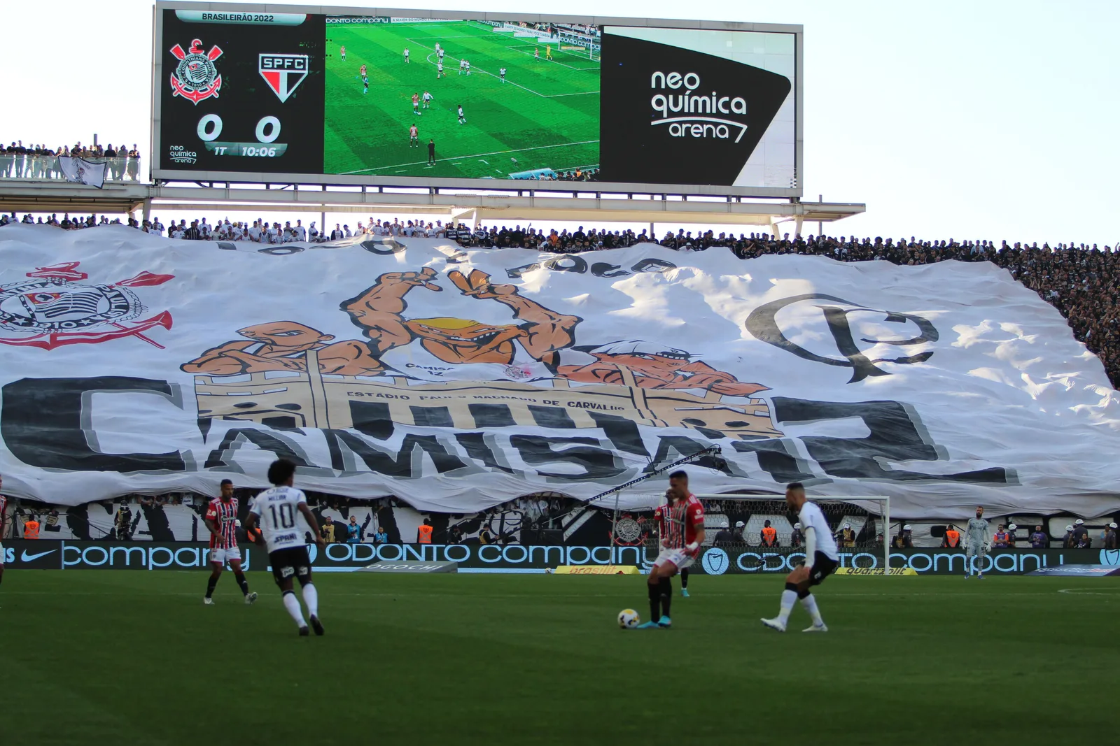 A giant banner unfurled across the whole home end at the Corinthians stadium during a match against São Paulo FC, the crowd holding it up behind the goal with the scoreboard showing the fixture above them