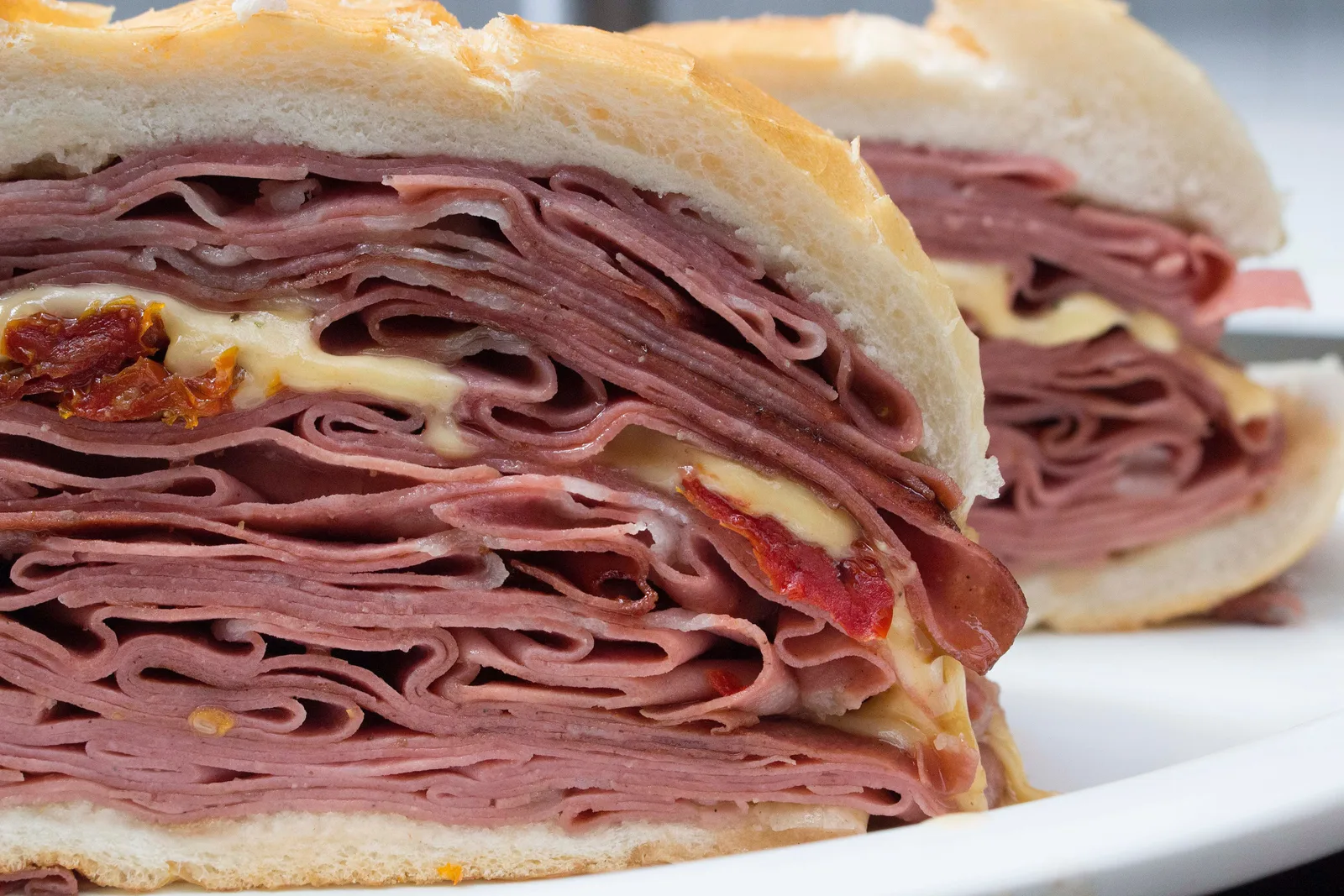 Close on a halved mortadella sandwich on a white plate, a thick fan of pink folded slices packed between two pieces of white bread with melted cheese at the edges