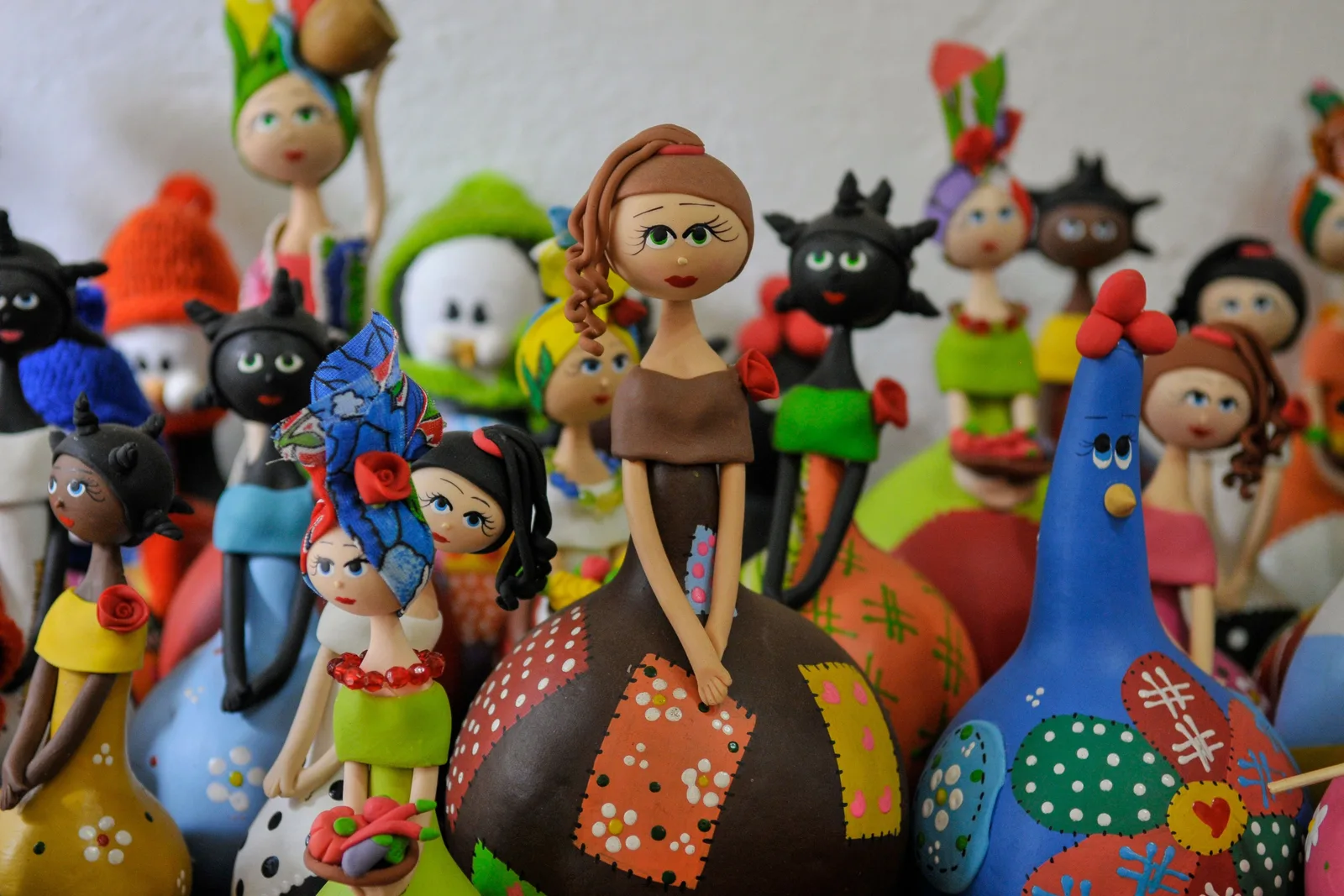 A crowd of brightly painted ceramic folk-art figures on a shelf in Tiradentes — women in patterned dresses, round-bodied dolls and black cats with wide eyes