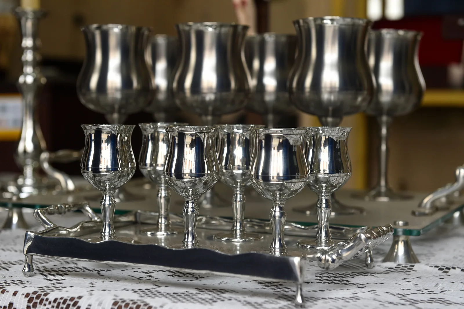 A row of polished pewter goblets standing on a tray in a São João del-Rei workshop, with more finished pieces out of focus behind them