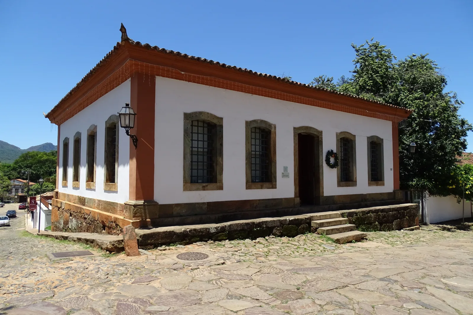 The old public jail of Tiradentes, now the Museu de Sant’Ana: a low white colonial building with dark red window frames and a hipped tile roof, standing on a cobbled corner