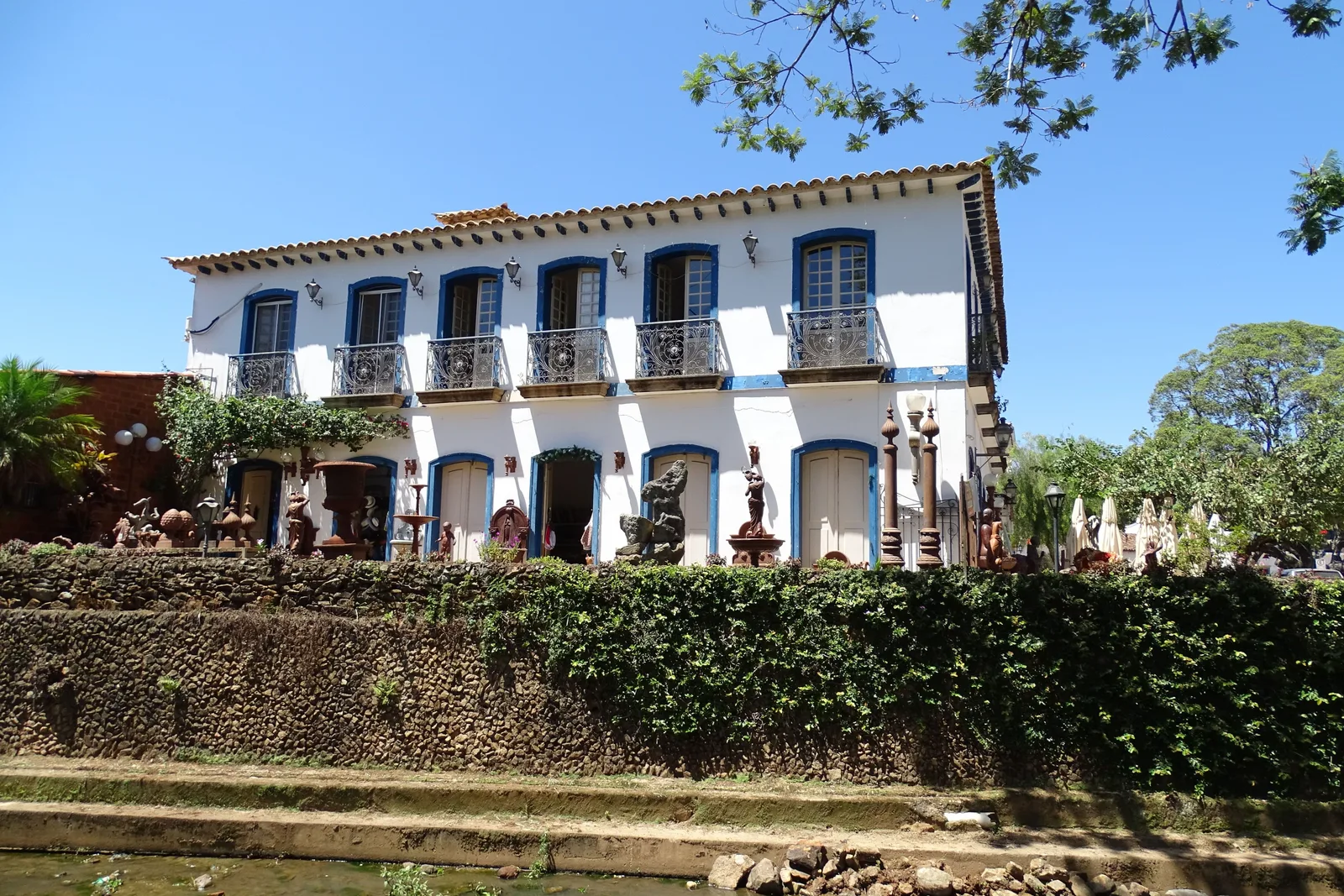 The old town hall of Tiradentes, a long white two-story building with a row of iron balconies, seen over the hedge and stalls in front of it