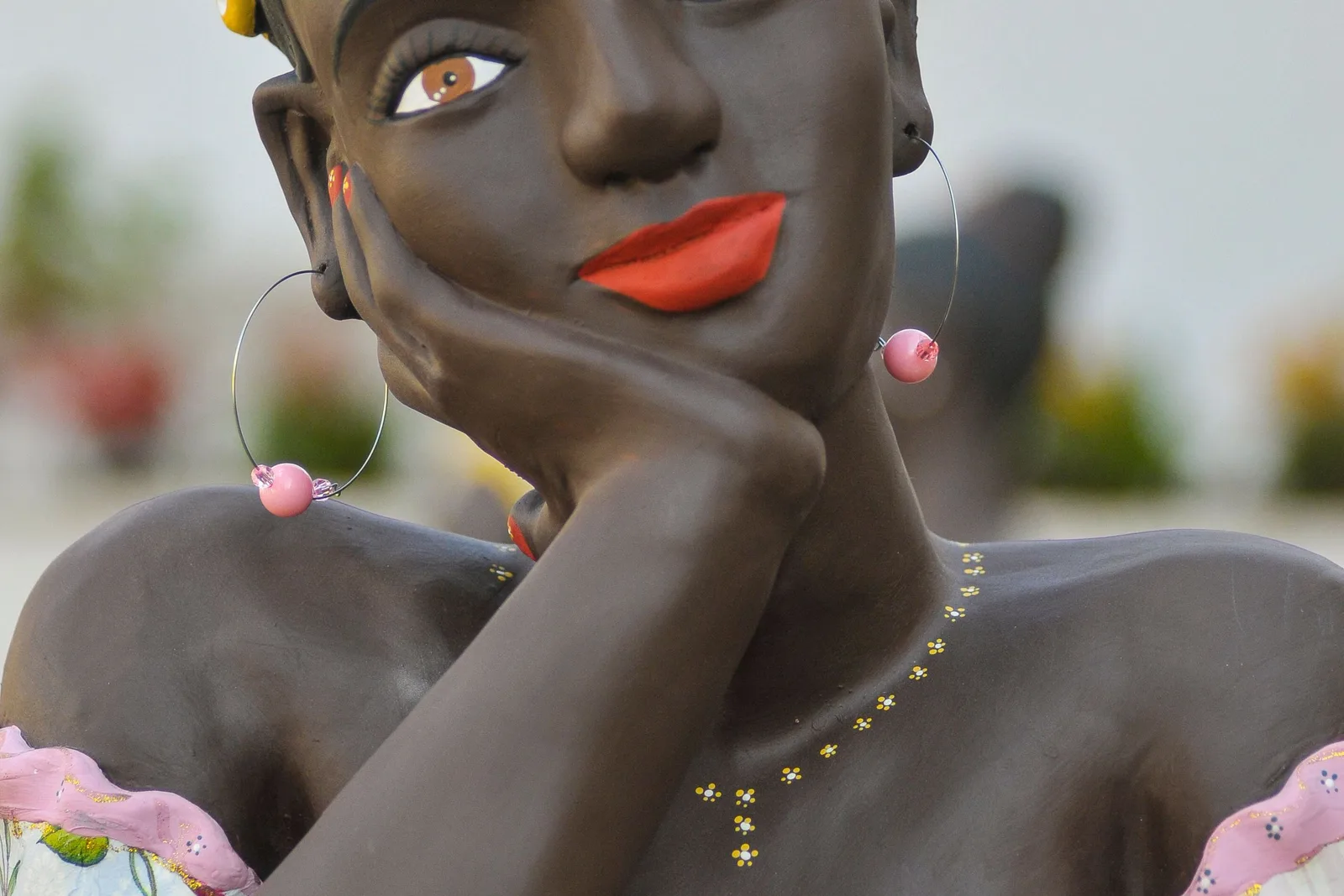 A dark ceramic bust of a woman resting her chin on her hand, painted with red lips, hoop earrings and a beaded necklace, on an artisan’s table in Tiradentes