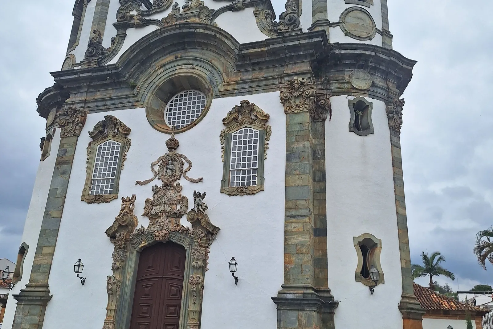 The carved soapstone portal of the Igreja de São Francisco de Assis in São João del-Rei, its rococo medallion and scrollwork set into a white plastered facade