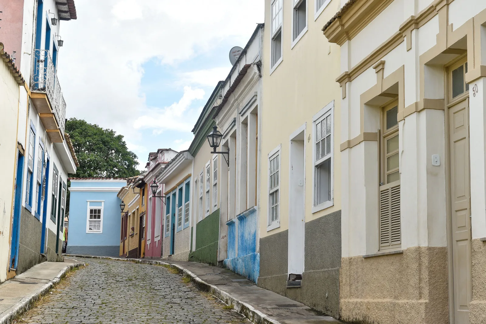 A narrow cobbled street in São João del-Rei lined with pastel-painted colonial houses in blue, cream and pink