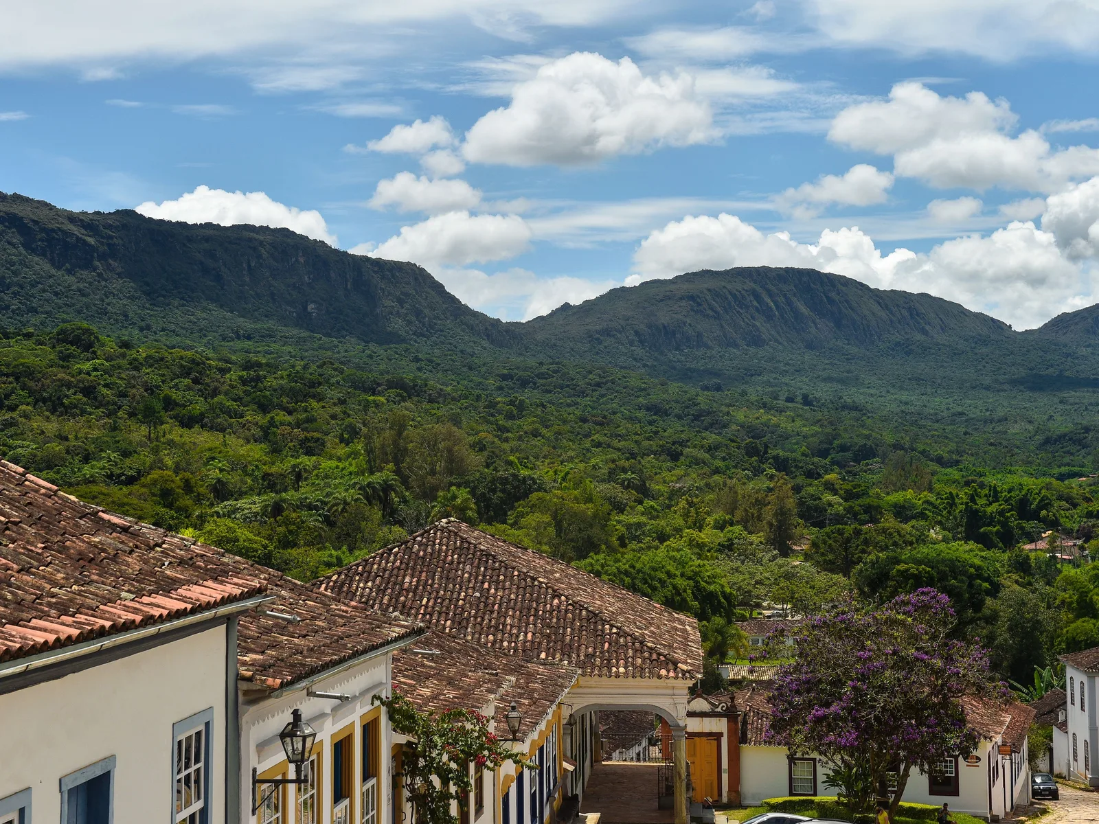 Looking out over the tiled rooftops at the edge of Tiradentes across a green valley of trees and pasture to the long forested ridge of the Serra de São José